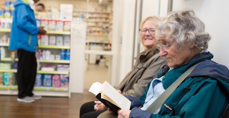 Two elderly women sitting in a pharmacy waiting for their prescription