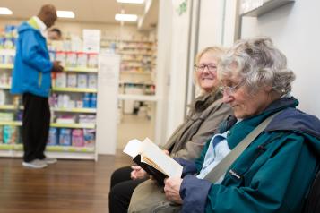 Two elderly women sitting in a pharmacy waiting for their prescription