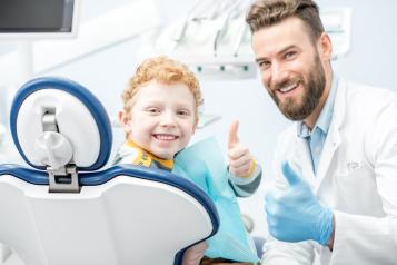 Dentist and happy boy showing OK sitting on the chair at the dentist